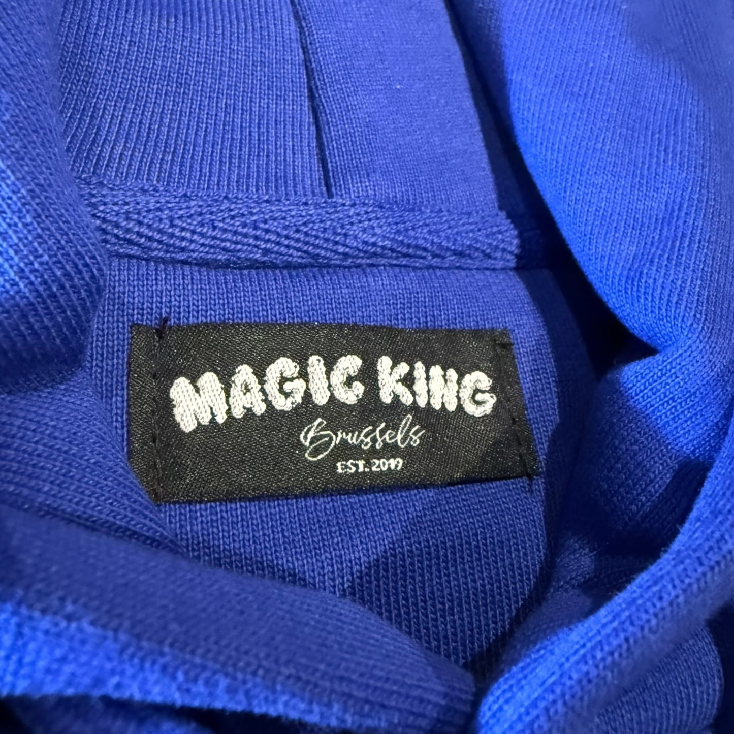 Hoodie Magic King White Ash Gang bleu royal avec logo joint Magic devant et imprimé White Ash Gang dans le dos. Confort et style premium. Etiquette cou.